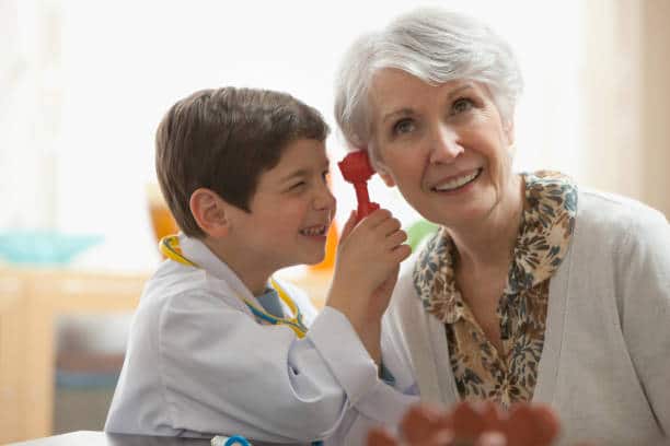 Petit garçon qui joue au docteur en faisant un examen auditif à sa grand-mère